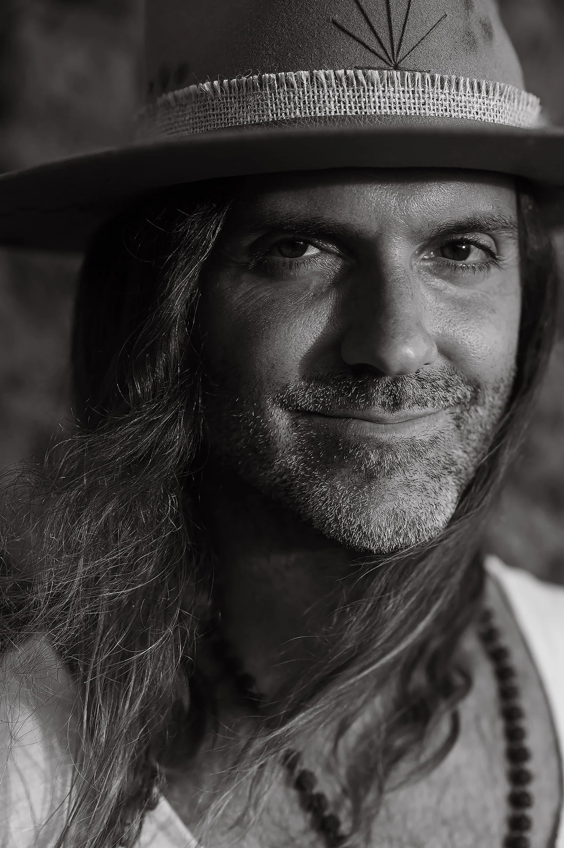 Black-and-white portrait of Daniel Bellone smiling at the camera beneath his wide-brim hat